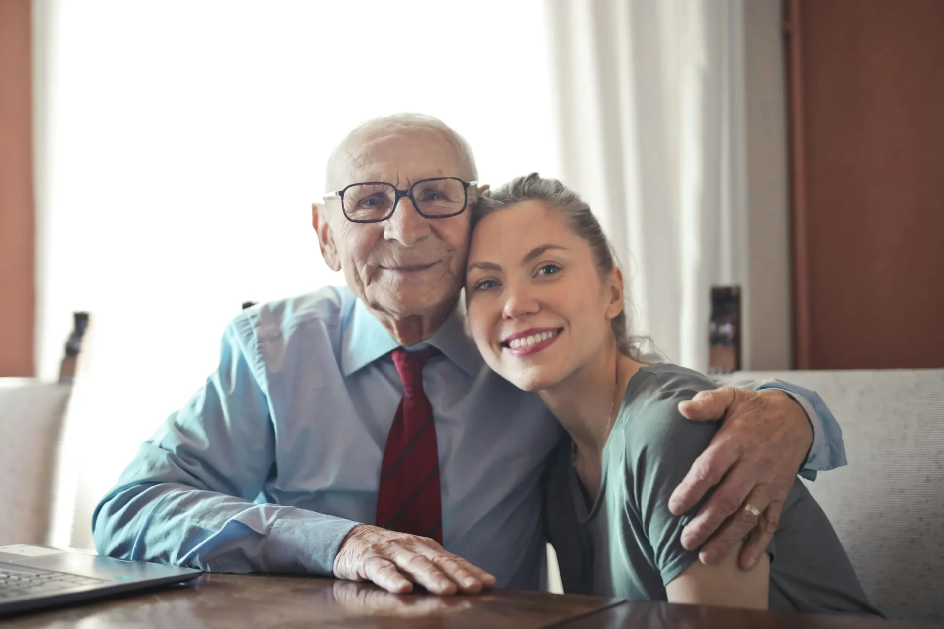 An elderly man and a young woman hugging at a table.